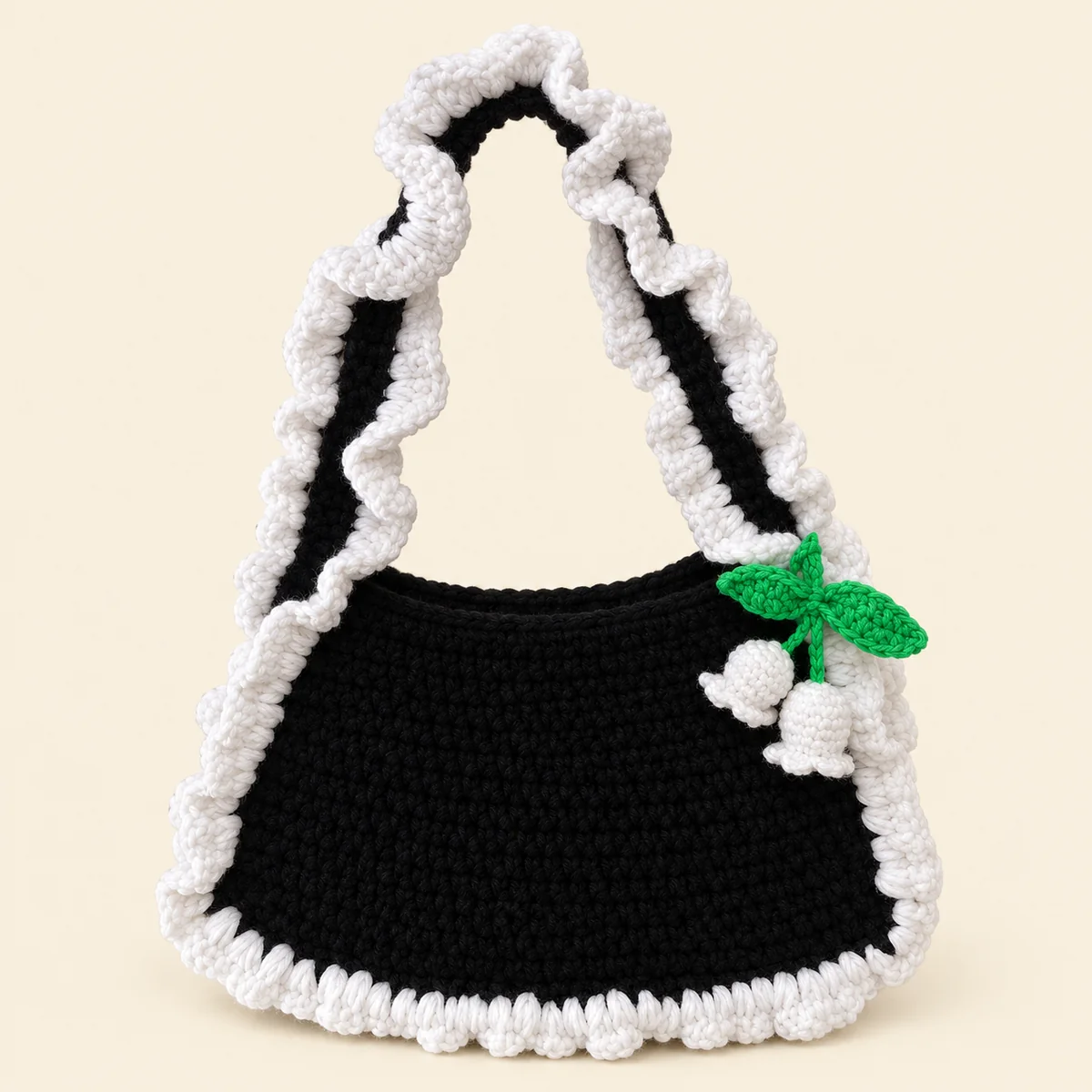 Handmade black crochet shoulder bag with white ruffle edging and a lily-of-the-valley charm
