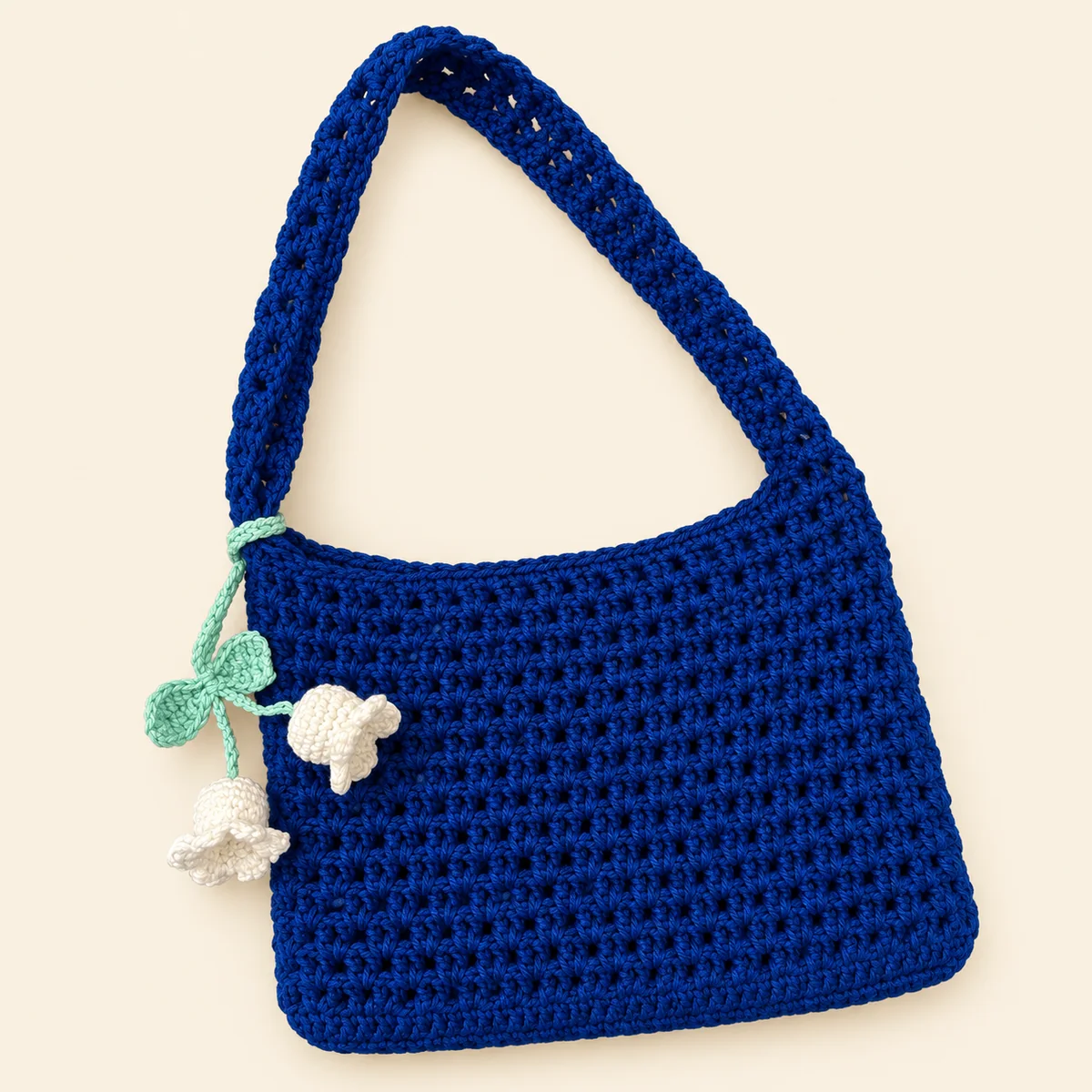 Handmade royal blue crochet shoulder bag with a white lily-of-the-valley charm