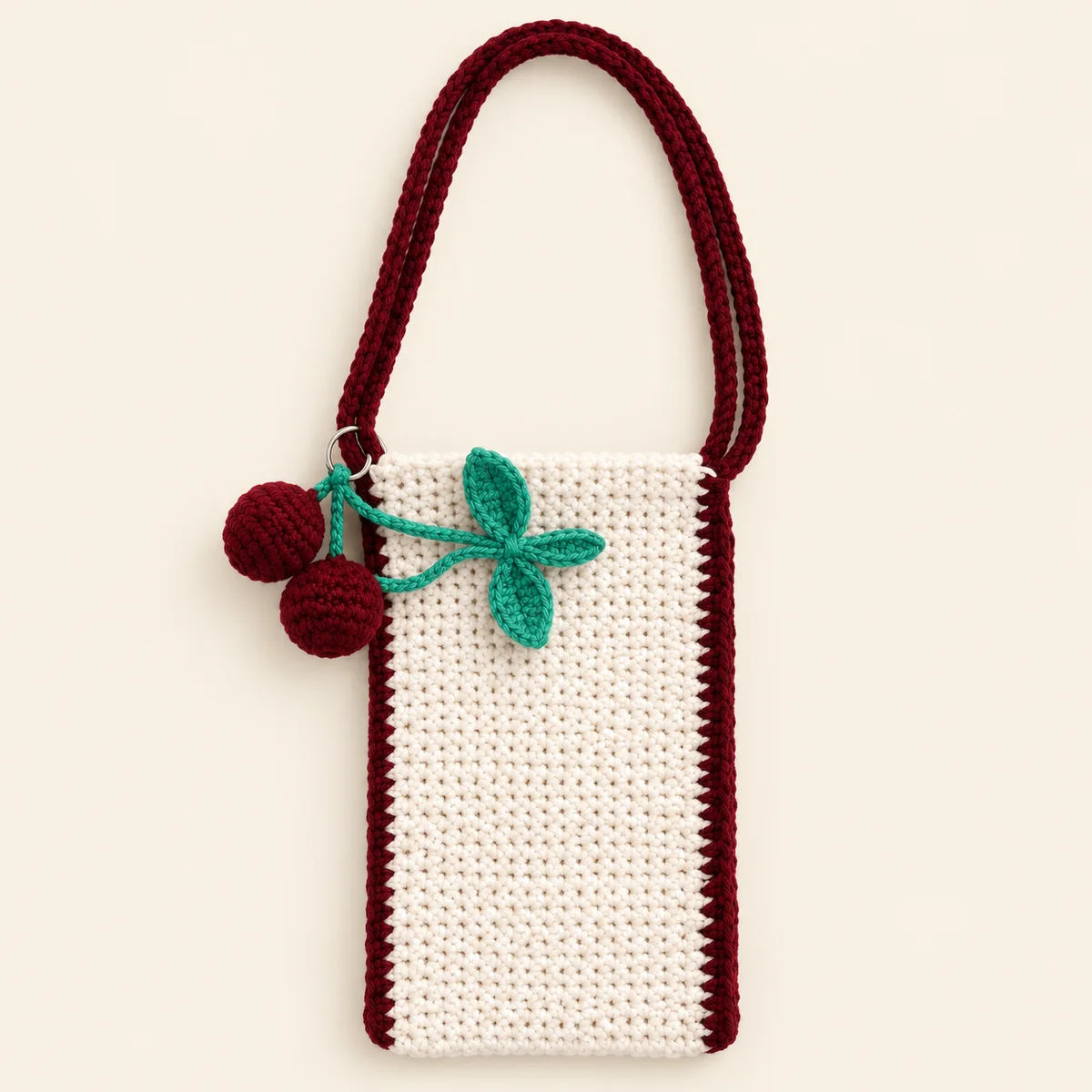 Handmade white crochet phone pouch with maroon trim, a maroon strap and a cherry charm